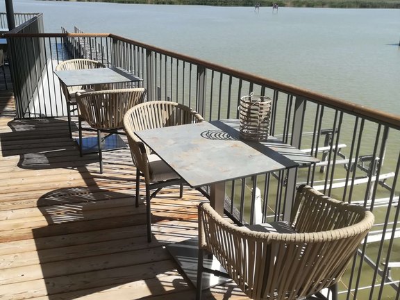 Blick von der Terrasse mit Stühlen und Tischen auf das ruhige Wasser des Sees